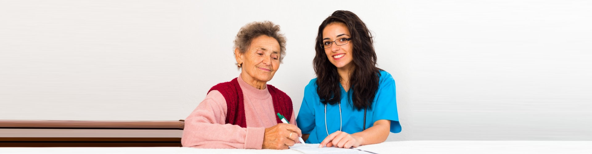 image of an elderly woman holding a pen with a female caregiver